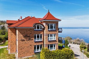 En tvåvåningsbyggnad i tegel med ett rött tegeltak, en balkong och utsikt över en sjö eller ett annat vattendrag.