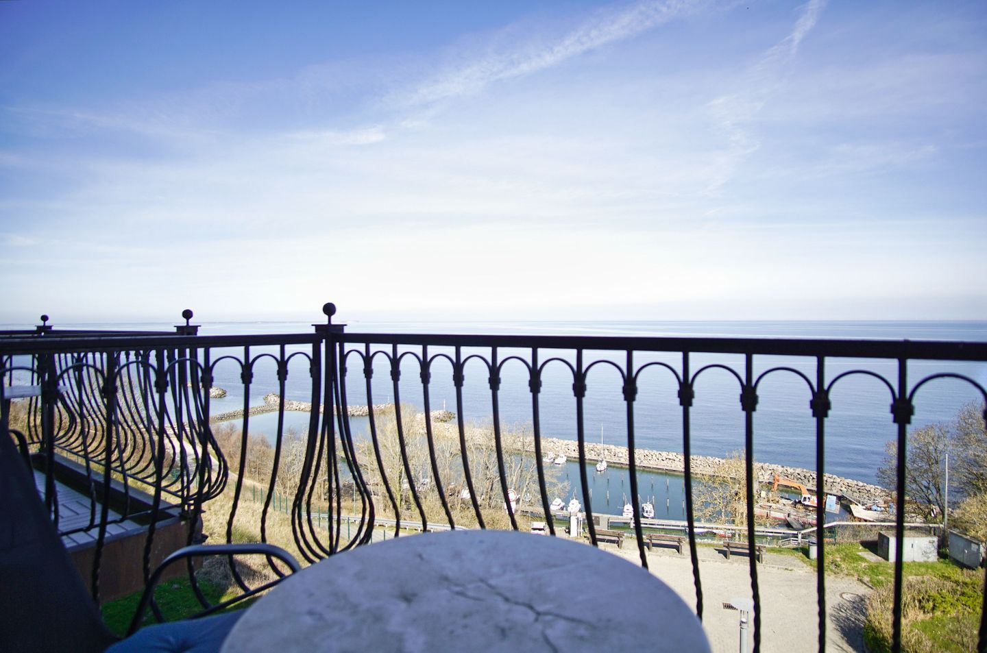 A balcony with a metal railing, a view of the sea, and boats anchored near the shore.