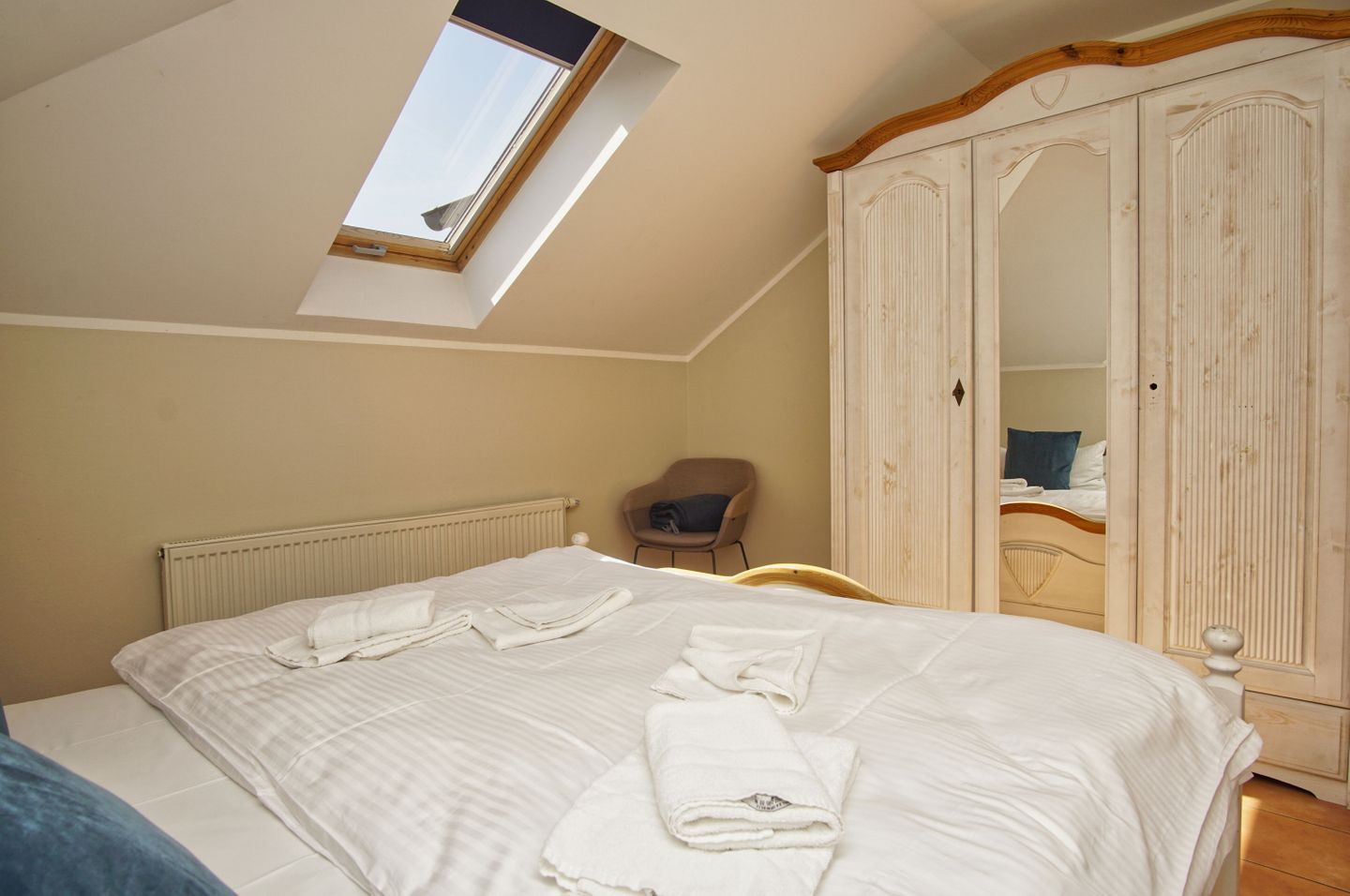 Ein Schlafzimmer mit Oberlicht, einem Bett mit ordentlich gefalteten Handtüchern, einem Sessel und einem Kleiderschrank.