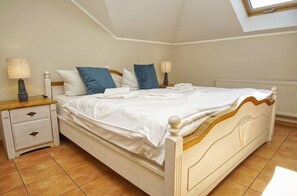 A bedroom with a bed, two bedside tables, a radiator, and a skylight.