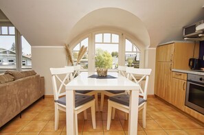 A modern kitchen with white cabinetry, a dining table with chairs, and a built-in oven. - Die Ferienwohnung Nr. 12 im Haus am Meer - Haus am Meer (Lohme)