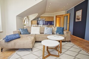 Ein modernes Wohnzimmer mit einem beigefarbenen Ecksofa, einem runden weißen Couchtisch und einer Küche im Hintergrund.