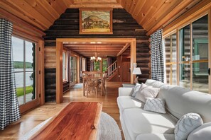 Ein Holzblockhaus-Interieur mit Essbereich, Sofa und großen Fenstern mit Blick auf einen See.