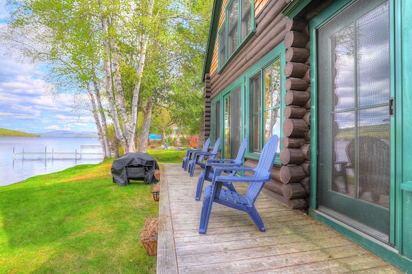 A log cabin with a porch, outdoor seating, and a view of a lake.