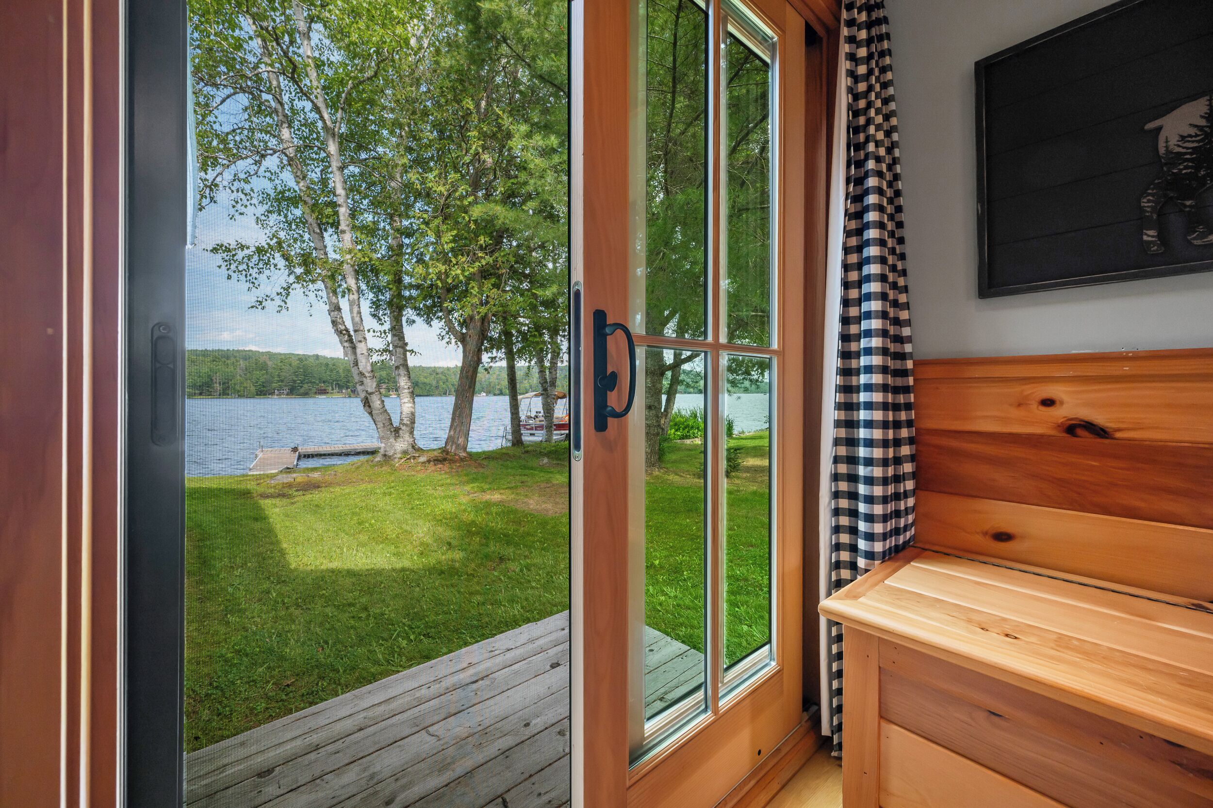 A wooden cabin with a sliding glass door leading to a deck overlooking a lake.