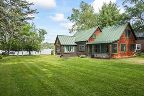 A cabin with a green metal roof, wooden siding, and a grassy yard. - The Lake Escape on Rangeley Lake (Rangeley)