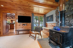 A wooden interior with a stone fireplace, a television mounted on the wall, and a bench. - The Lake Escape on Rangeley Lake (Rangeley)