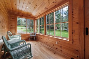 A cabin interior with wooden walls, large windows, and wicker furniture. - The Lake Escape on Rangeley Lake (Rangeley)