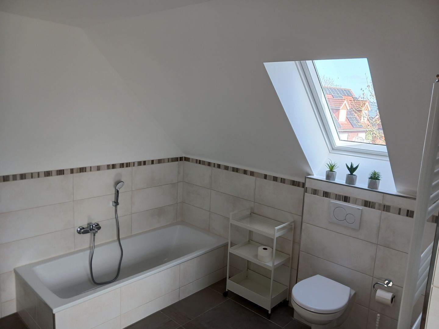 A modern bathroom with a bathtub, toilet, and skylight.