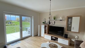 A modern living room with a large TV, a chandelier, and a sliding glass door to a balcony.