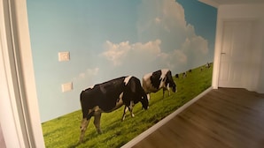 A room with a mural of cows on a green field under a blue sky.