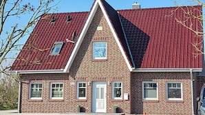 A two-story brick house with a red-tiled roof, a central chimney, and a small window with a blue sky view.