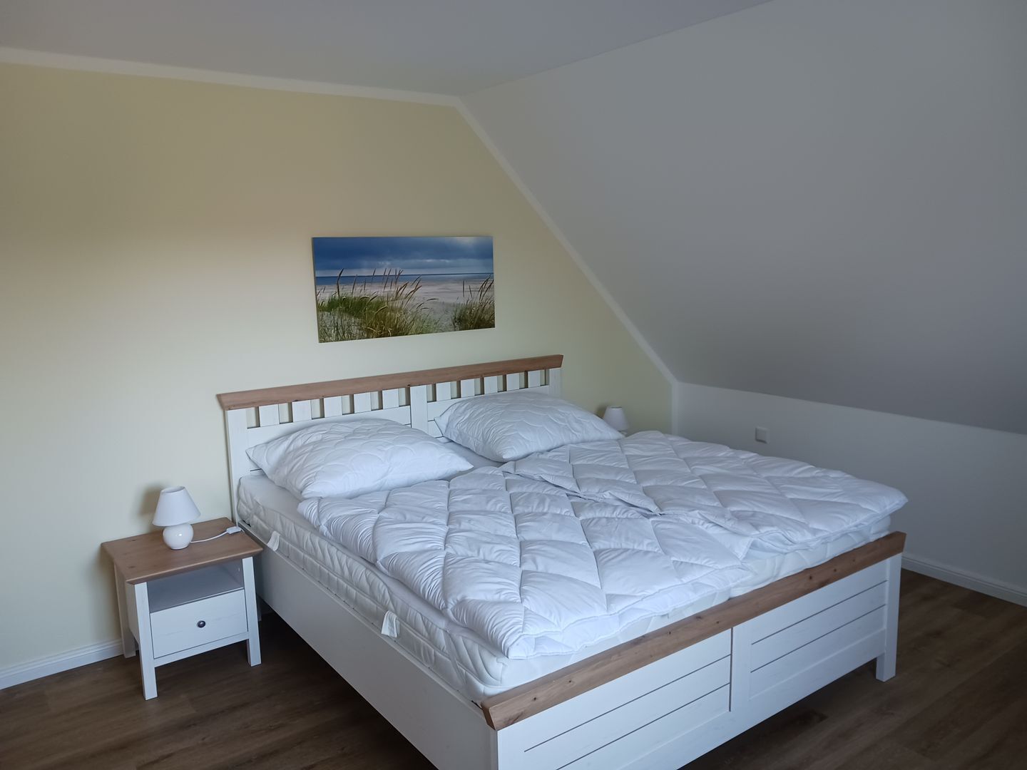 A bedroom with a bed, a nightstand, a lamp, and a painting on the wall.