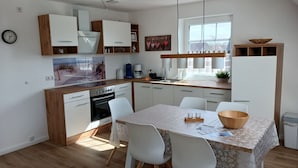 A modern kitchen with white cabinetry, a dining table with chairs, and a large window providing natural light.