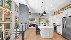 Een moderne keuken met een centraal eiland, grote ramen en een eethoek met uitzicht op groen.