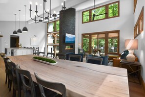 Enjoy meals in this dining area with a large table, modern chairs, and a high ceiling with pendant lights.