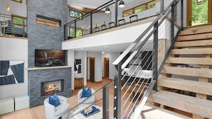 Een ruime woonkamer met een open haard, een trap en een balkon met zitplaatsen.