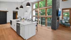 Een moderne keuken met een centraal eiland, hangende verlichting en grote ramen met uitzicht op de omgeving.