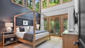 Een moderne slaapkamer met een hemelbed, een houten nachtkastje, een bijzettafeltje, een groot raam en uitzicht op de omgeving.