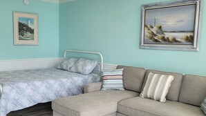 Quarto com cama, sofá, quadro emoldurado e piso de madeira.