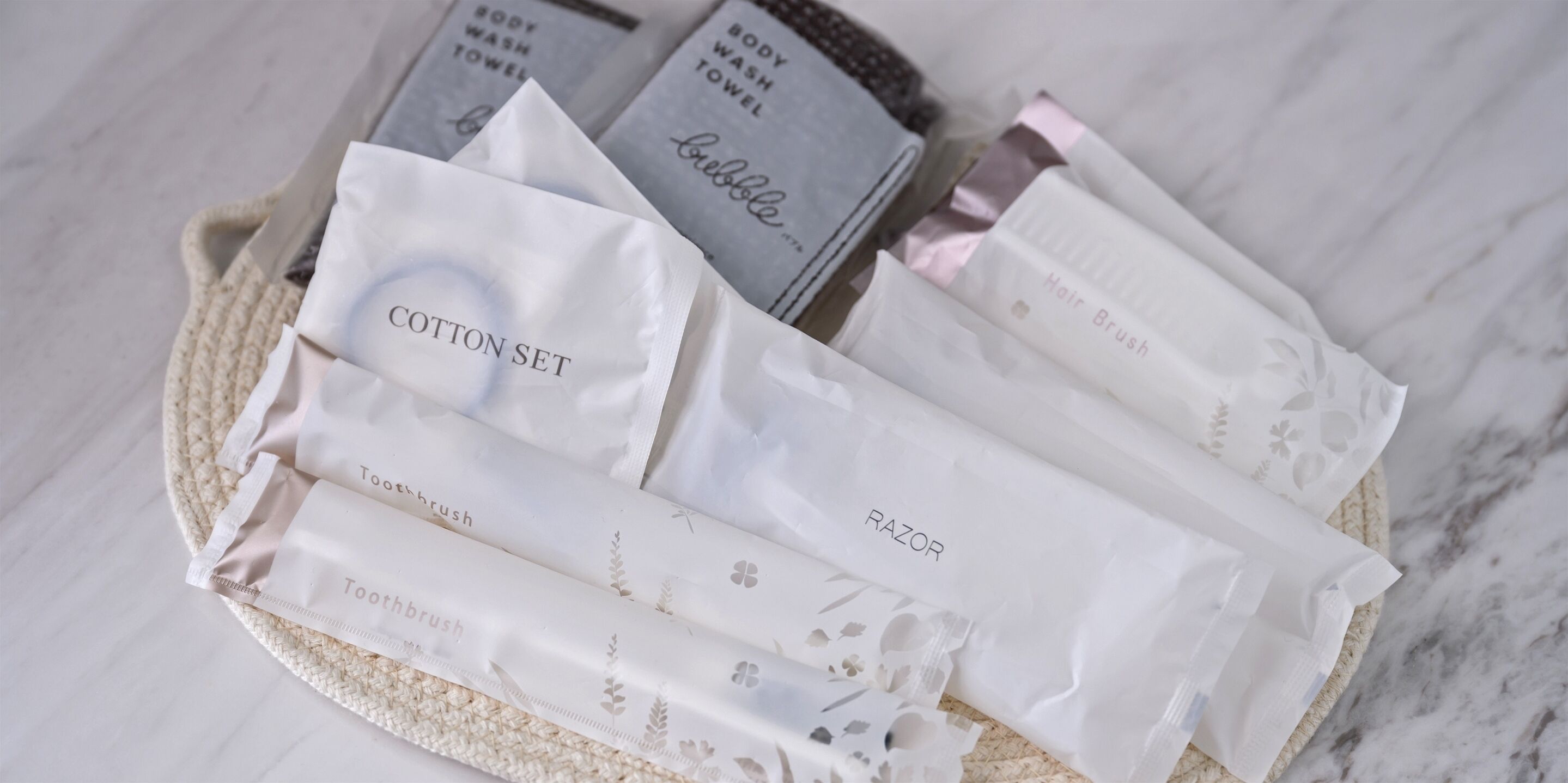 A basket containing various toiletry items including cotton set, razor, body wash towel, and hair brush.