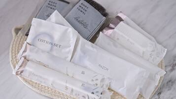 A basket containing various toiletry items including cotton set, razor, body wash towel, and hair brush.