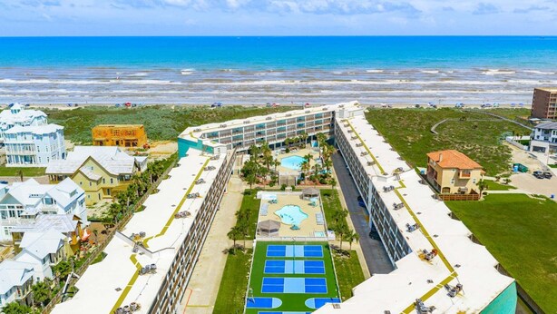 A hotel with a pool, a beach view, and a tennis court.