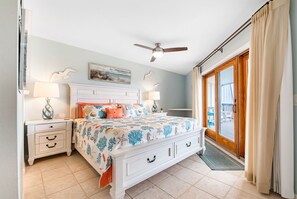 Une chambre à coucher avec un lit, des tables de chevet, un ventilateur de plafond et une vue sur l’extérieur.