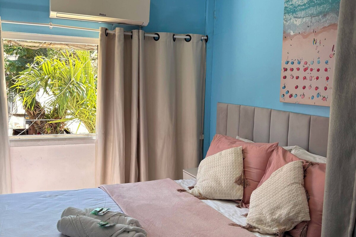 A bedroom with a bed, pillows, a blanket, a window with curtains, and a wall-mounted air conditioner.