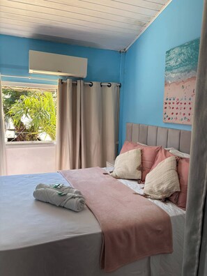 A bedroom with a bed, pillows, a blanket, a window with curtains, and a wall-mounted air conditioner.