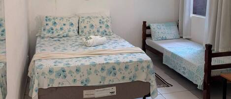A bedroom with a bed, a bench, a window with curtains, and wall-mounted hats.
