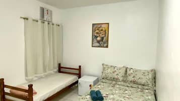 A small, clean room with a bed, a nightstand, a heater, and a painting on the wall.