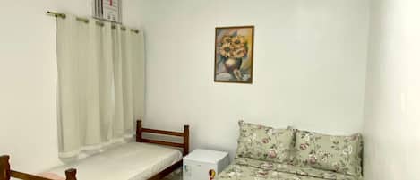 A small, clean room with a bed, a nightstand, a heater, and a painting on the wall.