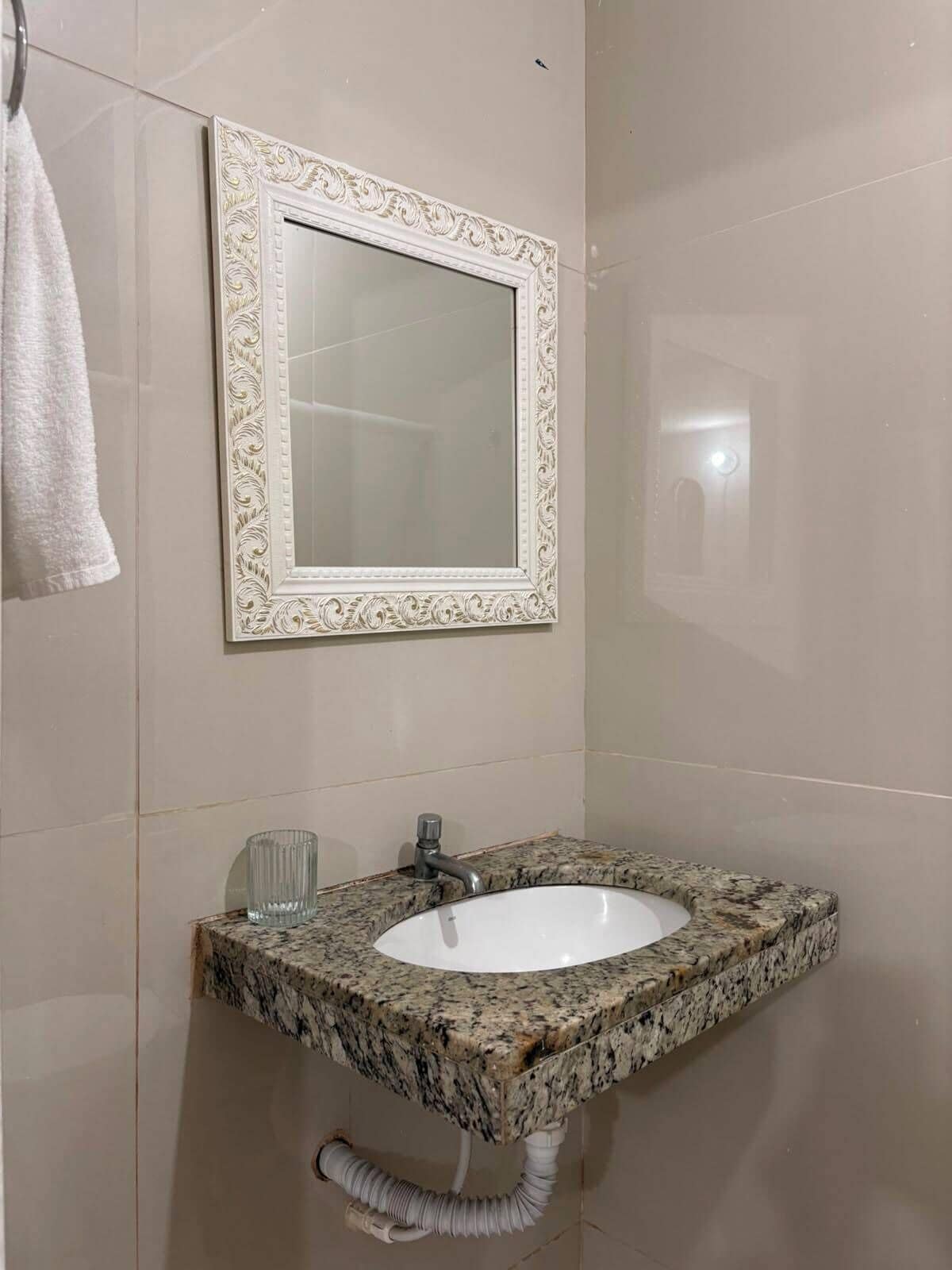 A bathroom with a marble sink, a wall-mounted mirror with an ornate frame, and a towel hanging on the wall.
