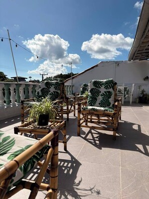 Une terrasse sur le toit avec deux fauteuils en osier, une petite table ornée d’une plante et une rambarde blanche.