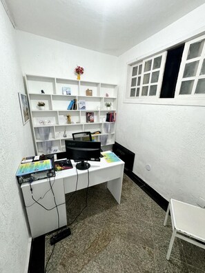 Una habitación pequeña con paredes blancas, un escritorio, estanterías y una ventana.