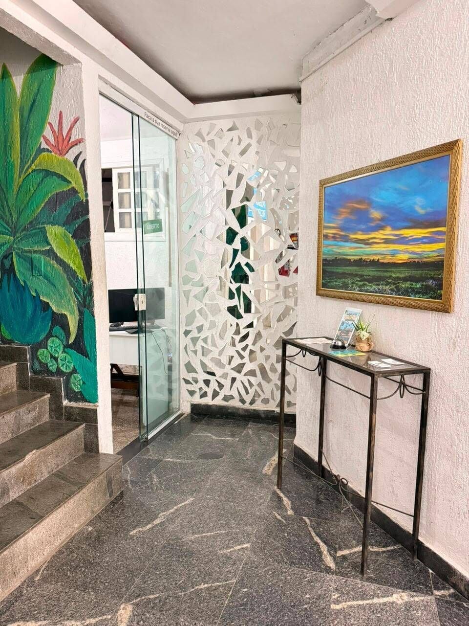 A hallway with a glass door, a decorative white wall, a framed painting, and a console table with a plant.