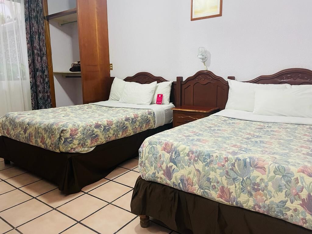Two twin beds with floral bedding, a wooden headboard, a nightstand, a telephone, and a wall-mounted fan.