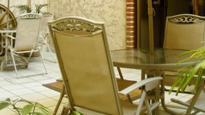 Una mesa redonda con tapa de vidrio, rodeada de sillas color beige con estructura metálica. Un paraguas ofrece sombra sobre la mesa.
