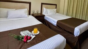 Una habitación de hotel con dos camas, una mesita con un periódico y un vaso de jugo de naranja, y una lámpara fijada a la pared.