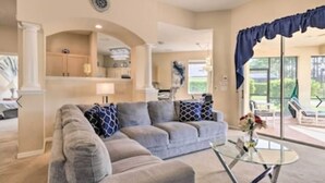 A living room with a grey sectional sofa, a glass coffee table, and a view of the outdoor patio.