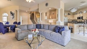 A spacious living room with a grey sectional sofa, a glass coffee table, and a staircase leading to the upper floor.
