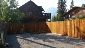 A fenced backyard with a gravel surface, a wooden deck, and a cabin with a balcony. - The Cedar - Downtown, walking distance to all the shops and restaurants! (Banff)
