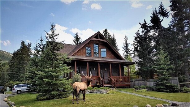 A lodge with a wooden exterior, a porch, and a large elk statue in the front yard. - The Cedar - Downtown, walking distance to all the shops and restaurants! (Banff)