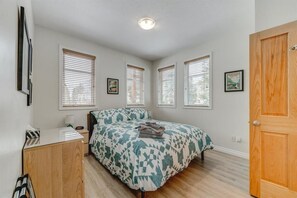 Quarto com cama, escrivaninha e guarda-roupa. Há quatro janelas com persianas e uma porta visível à direita.