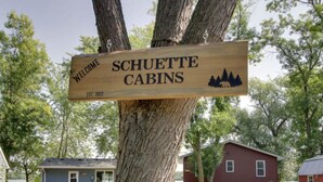 Een houten welkomstbord voor Schuette Cabins, opgericht in 2022, met cabins op de achtergrond.