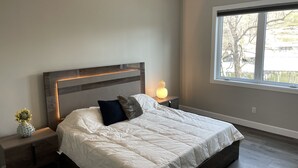 Ein Schlafzimmer mit einem großen Bett, einem Nachttisch mit Lampe, einem Deckenventilator und einem Fenster mit Blick auf Bäume.
