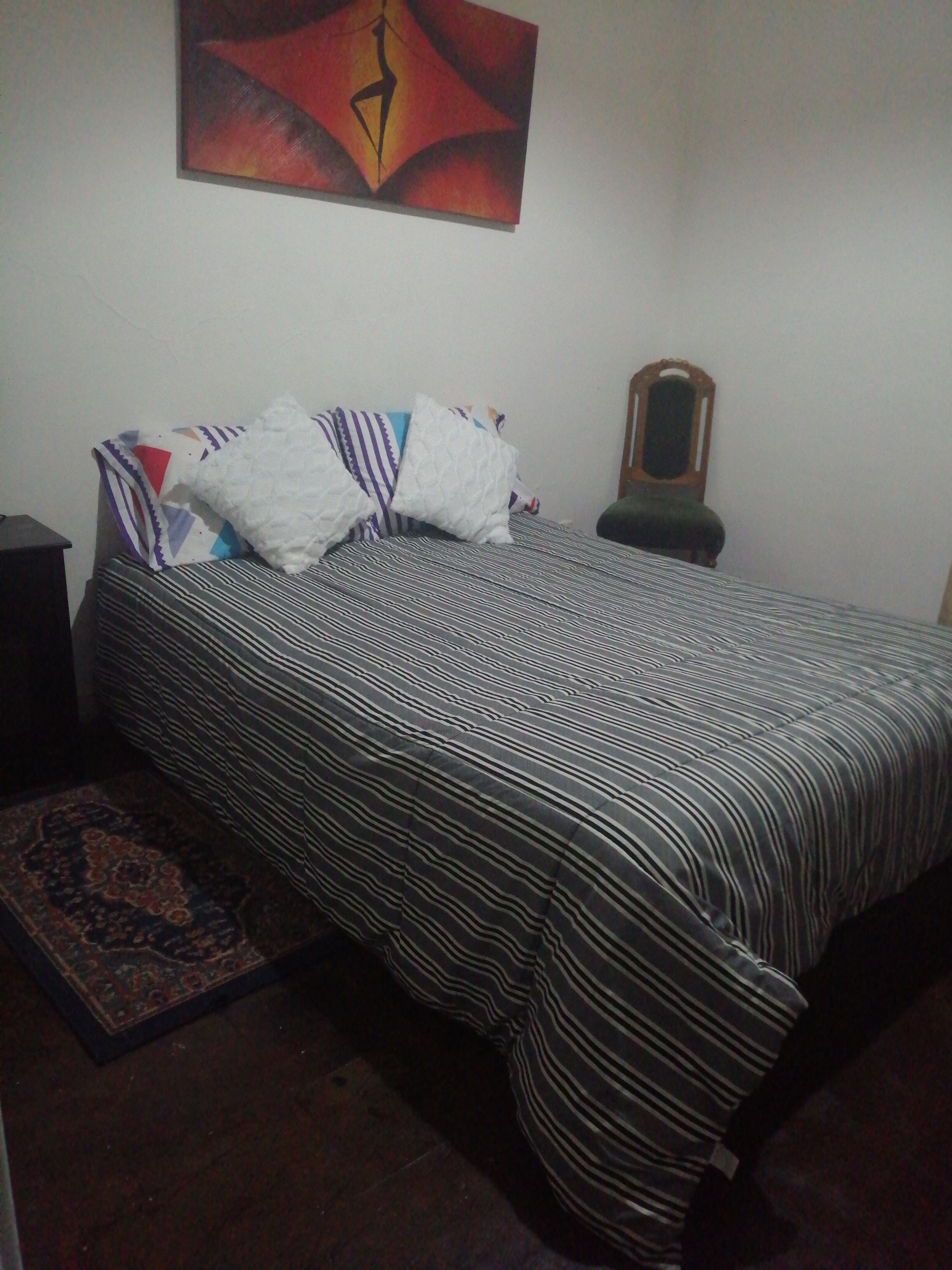 A bed with striped bedding, a patterned rug, a wall clock, and a framed picture.