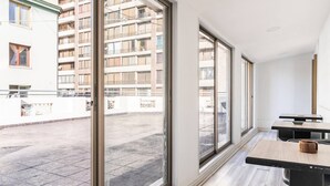 A modern interior with large windows, a wooden table, and a view of a residential building. - Hostal mancora (Santiago)