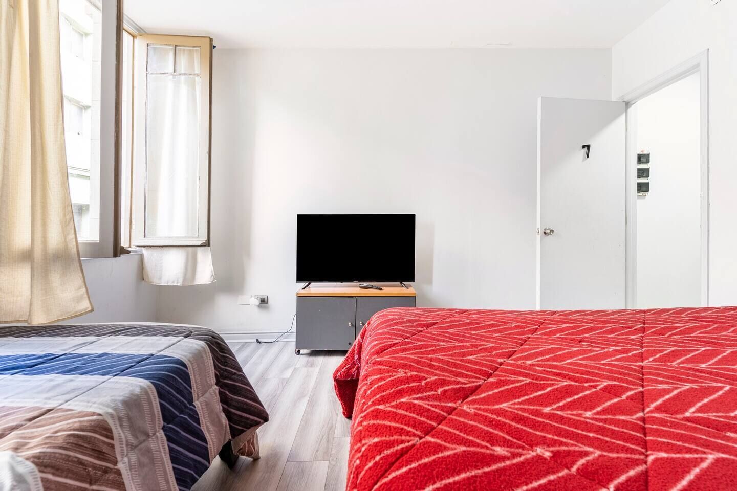 Ein Hotelzimmer mit zwei Betten, einem Fernseher auf einem Schrank, einem Kleiderschrank und einer Tür mit einer Nummer.